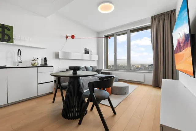 Svetlá obývačka s kuchynskou linkou, jedálenským stolom a výhľadom na Bratislavu z 28. poschodia apartmánu Skypark